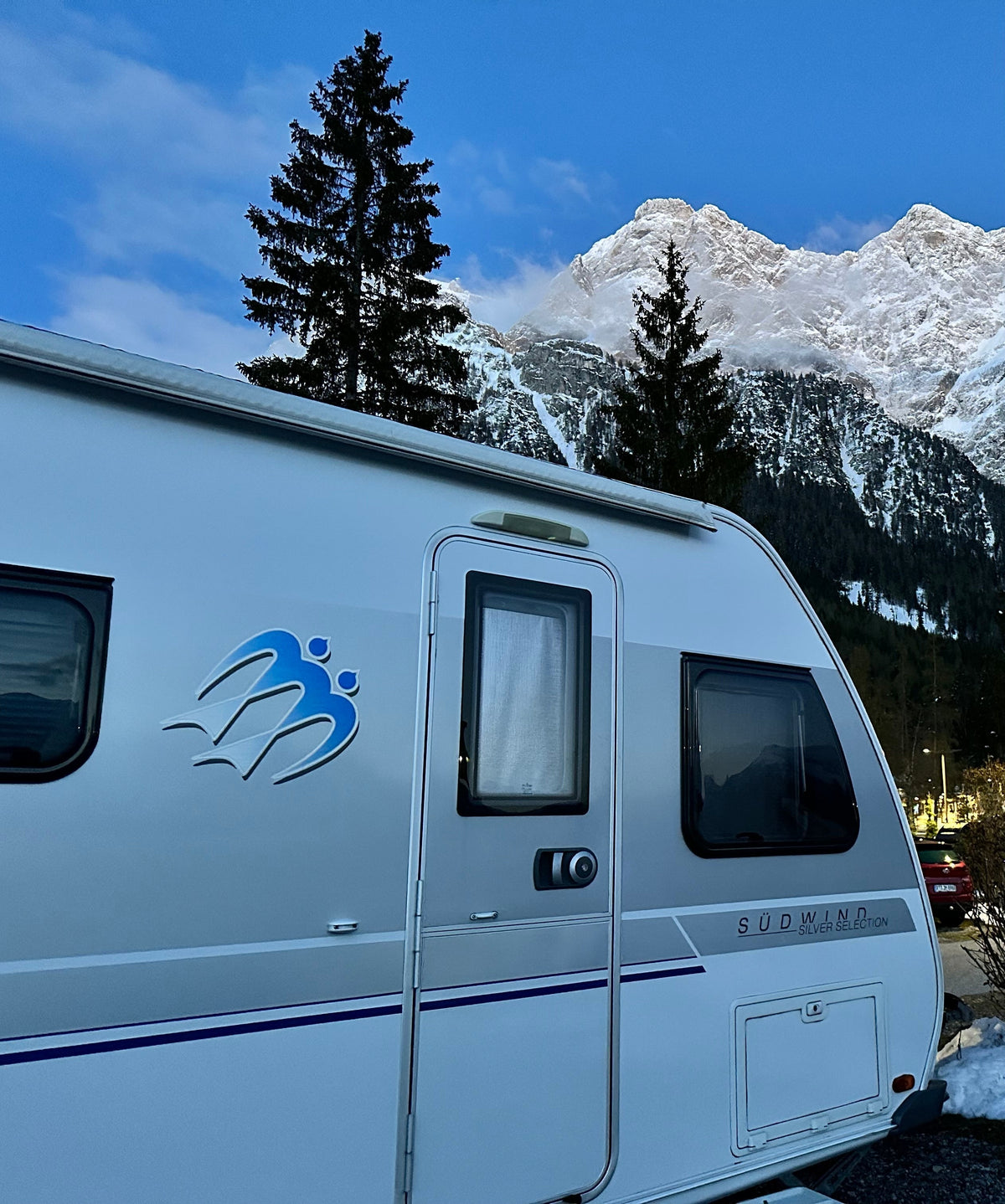 Wohnwagen auf dem Campingplatz vor verschneiten Bergen im Winter